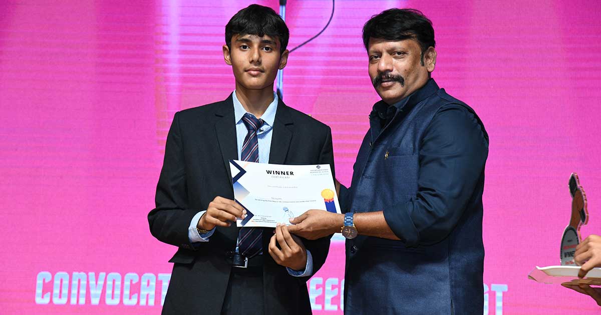 Young man in a suit and older man in a vest present a 'WINNER' certificate at JIRS Convocation.