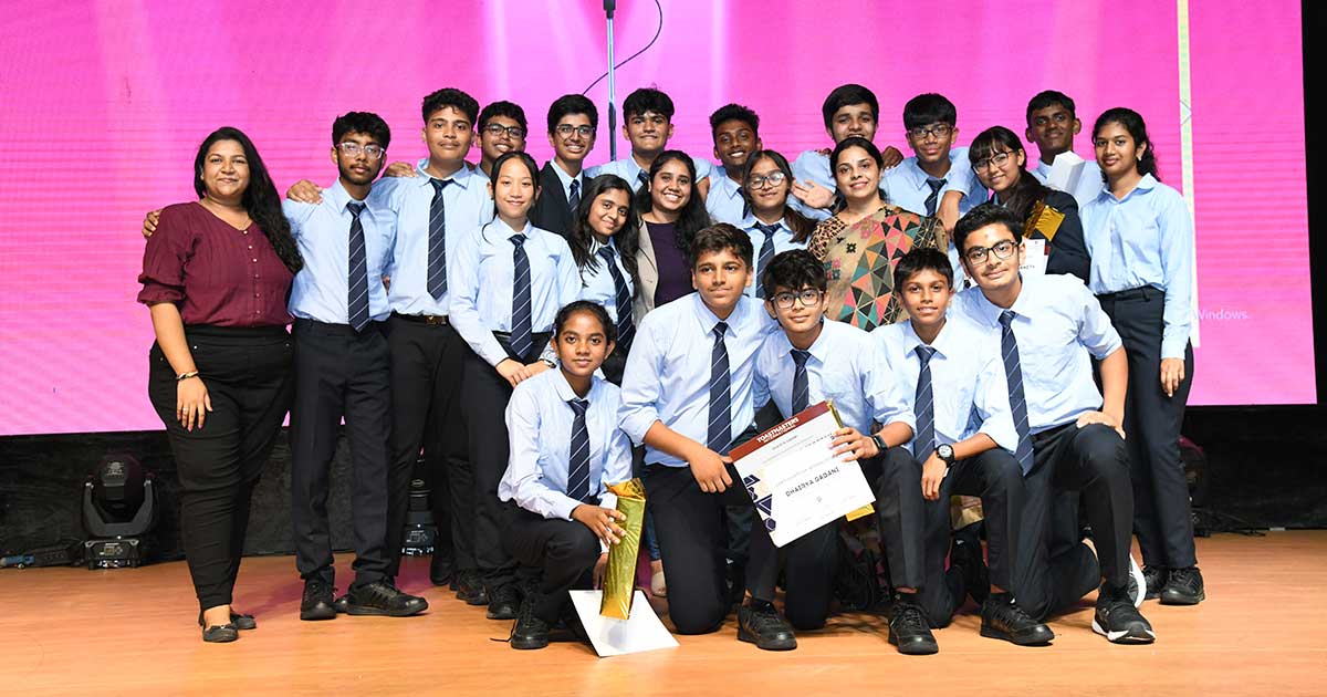 Group of students in formal attire celebrating on stage with a certificate and trophy at JIRS.