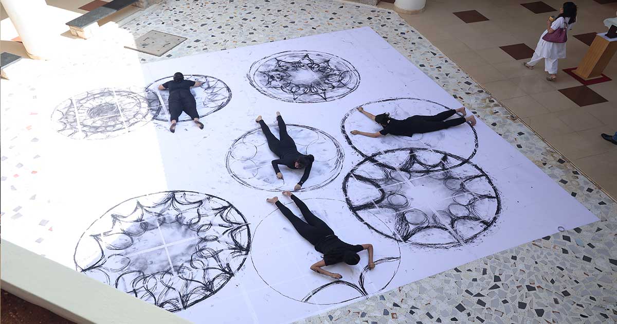 Participants in black engage in collaborative body art on a large paper at Afflatus 2023 indoor event.