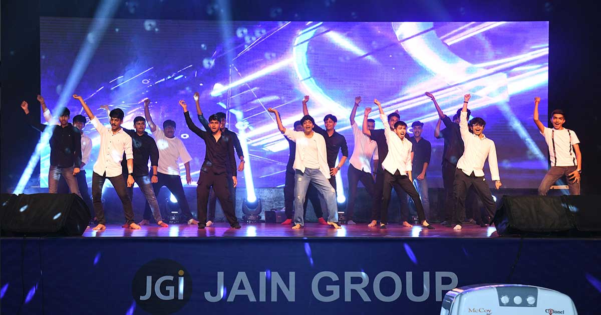 Young men in black and white outfits dance energetically on stage at JIRS Teacher’s Day event.