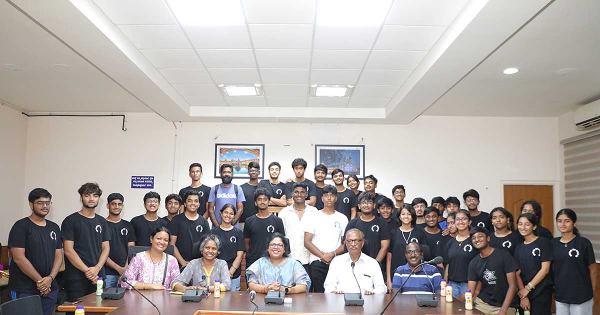 A large group in matching black T-shirts poses in a conference room during the IBDP Year 2 CAS Trip.