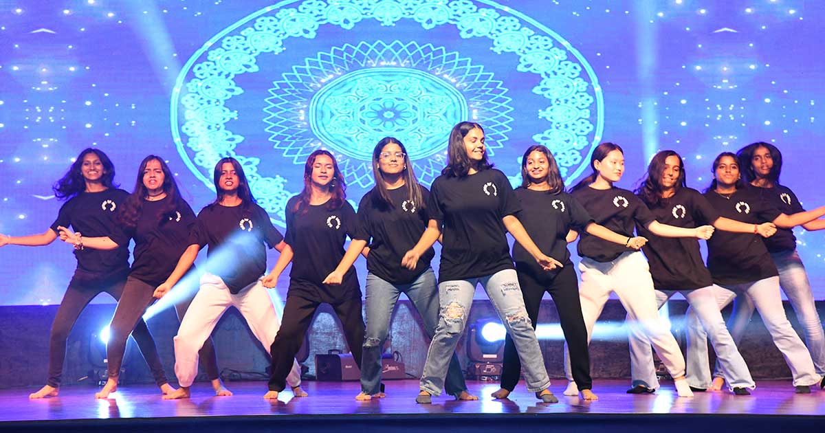 Young women in black t-shirts dance energetically on stage during JIRS Teacher’s Day celebrations.